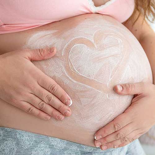 A pregnant woman cradles her bump, which has been smeared with cream, in which a loveheart has been drawn. This page is for stretchmarks, one of the skin conditions treated at The Women's Clinic