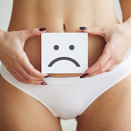 A close up of a woman's waist. She is holding a card with a sad face drawing. This page is for Vaginal Rejuvenation, one of the Menopause-related treatments at The Women's Clinic