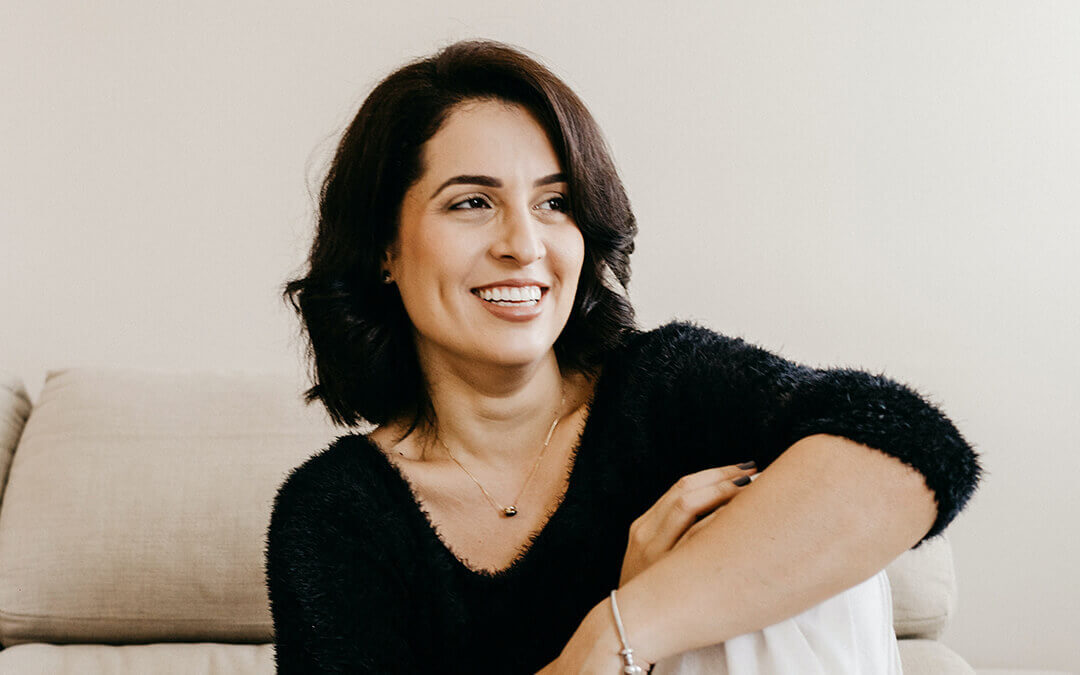 photo of a woman sitting at home, smiling as she looks off to the right of the frame.