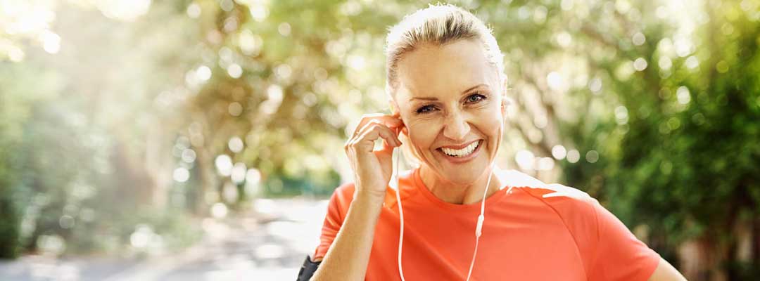 A promotional image for Urolon Stress Urinary Incontinencetreatment. It shows a happy elderly woman in a country lane. She is wearing headphones and seems to be out for a run.