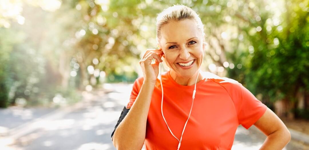 A promotional image for Urolon Stress Urinary Incontinencetreatment. It shows a happy elderly woman in a country lane. She is wearing headphones and seems to be out for a run.