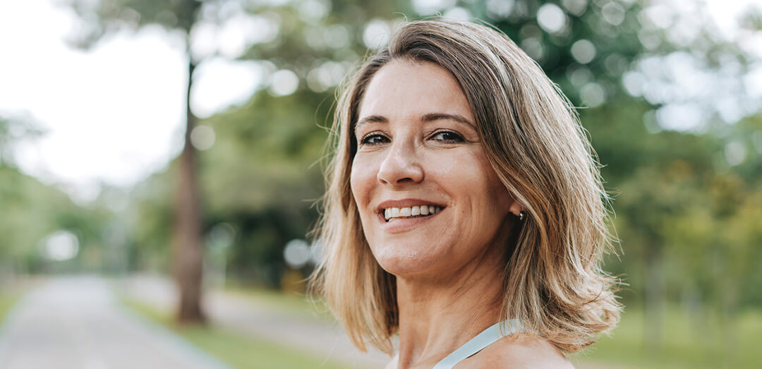 Vaginoplasty-image-A-1080x523-v01 A middle aged woman in a park, smiling at the camera