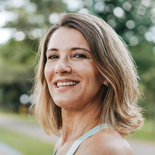 A middle aged woman in a park, smiling at the camera