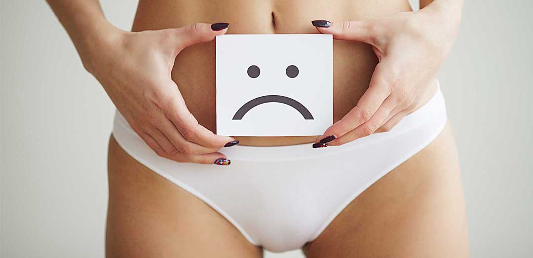 A close up of a woman's waist. She is holding a card with a sad face drawing. This page is for Vaginal Rejuvenation, one of the Menopause-related treatments at The Women's Clinic